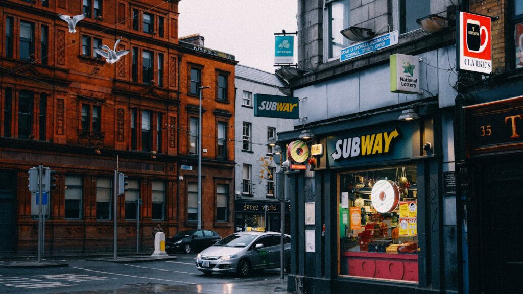 Busy urban street with Subway shop and historic architecture.