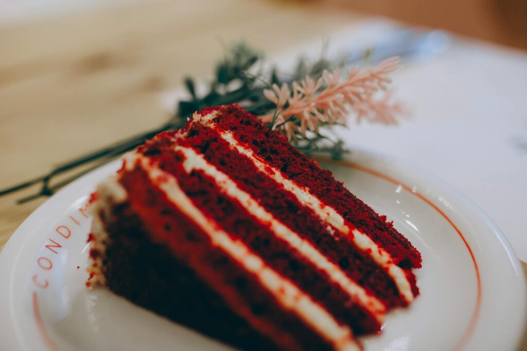 A slice of red velvet cake with creamy layers on a white plate, perfect for dessert lovers.