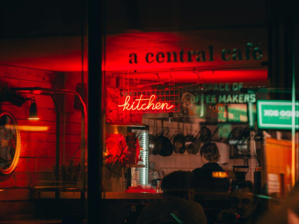 Warm and inviting photo of a Budapest café with a neon kitchen sign and atmospheric lighting.
