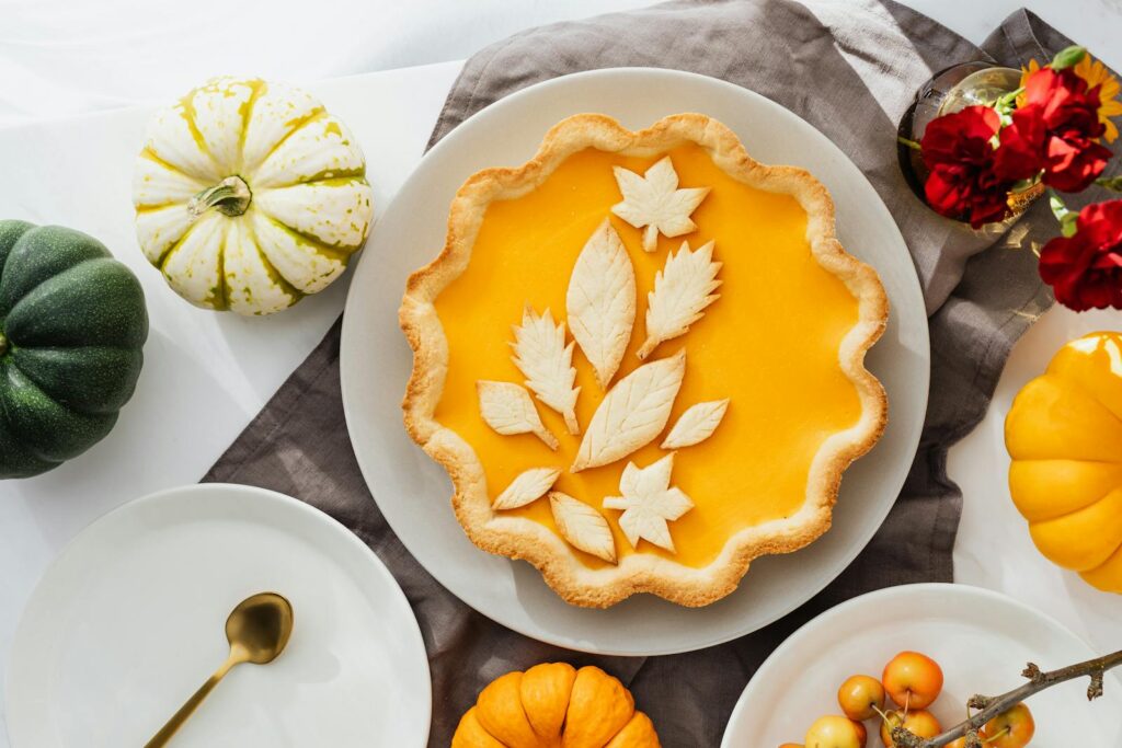 Flat lay of a pumpkin pie with leaf-shaped pastry decorations, surrounded by small pumpkins and flowers.