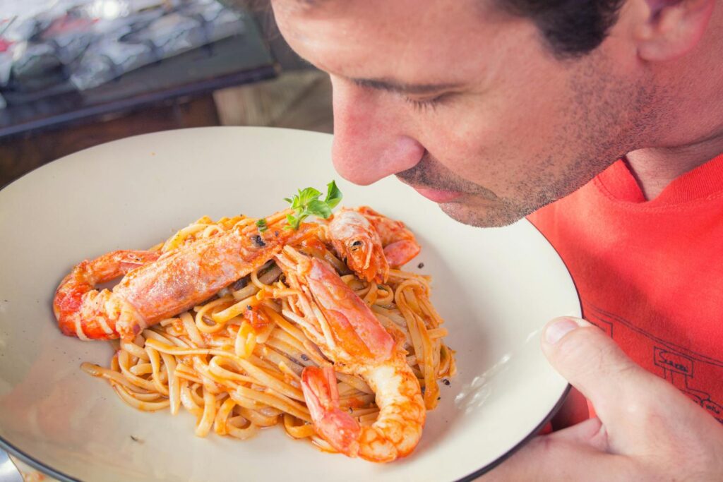 A man enjoys the aroma of a shrimp pasta dish with herbs. Perfect for food lovers.