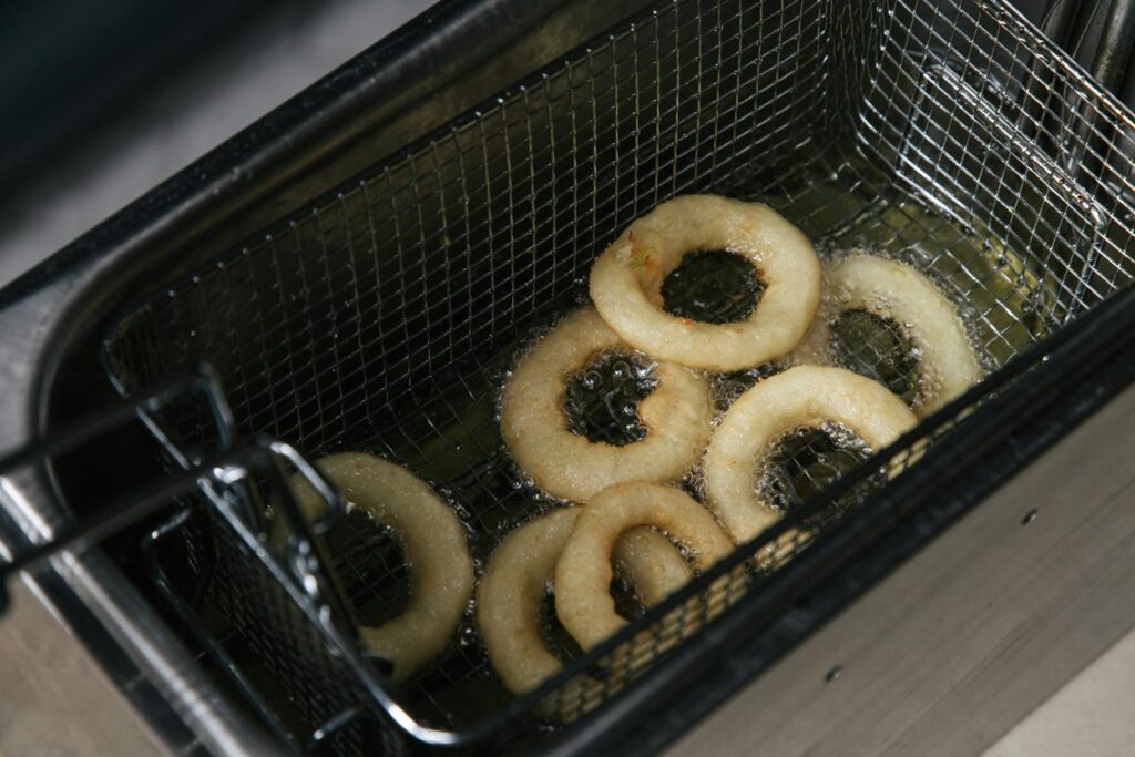 Hot crispy onion rings frying in oil in a deep fryer. Perfect food photography shot from above.