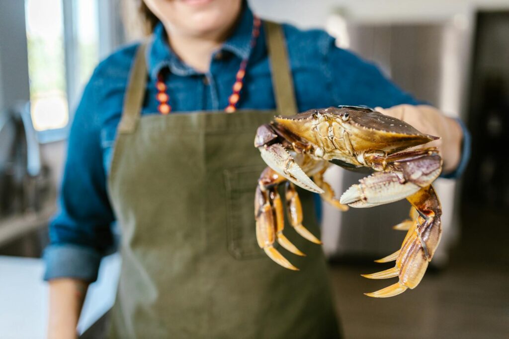 Woman in apron holding a live crab in a kitchen setting, showcasing fresh seafood.