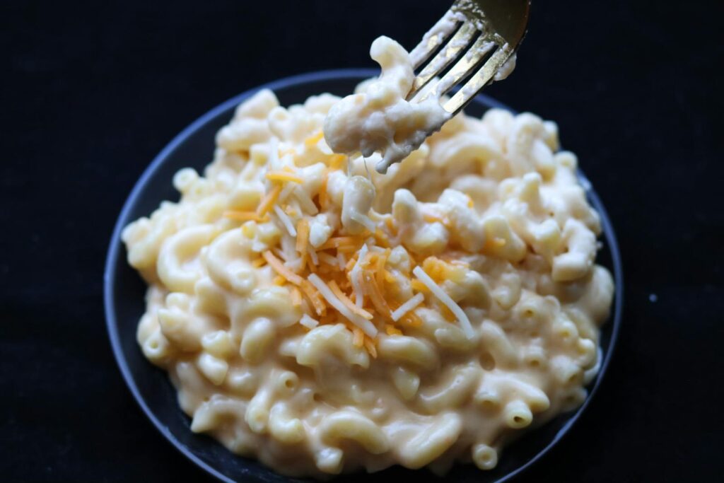 Delicious creamy mac and cheese topped with shredded cheese on a black plate.