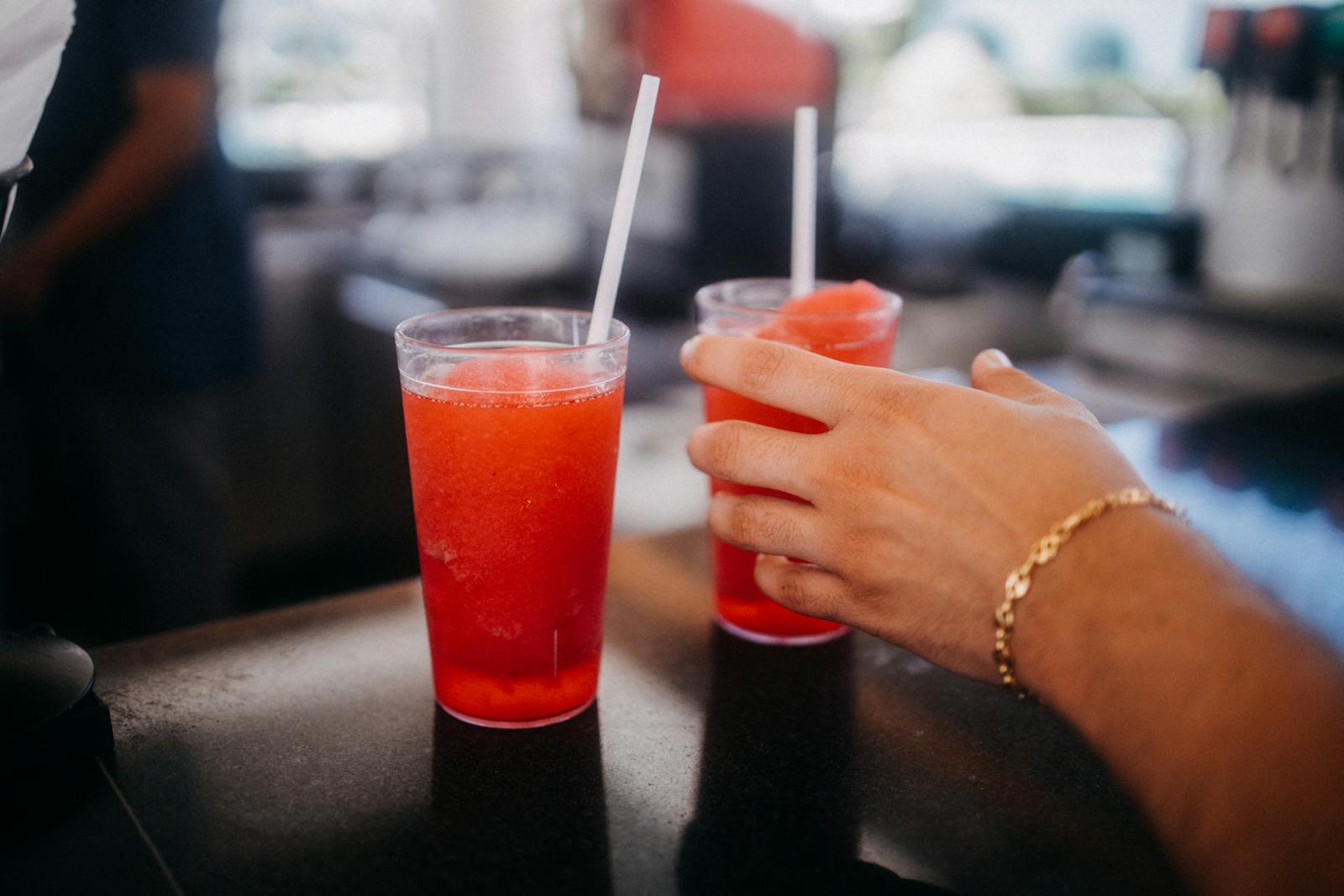 Close-up of a hand reaching for a red slushie drink in a restaurant setting.