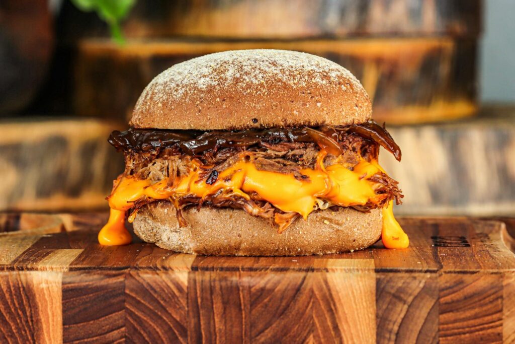 Delicious pulled pork burger with melted cheese on a wooden board.