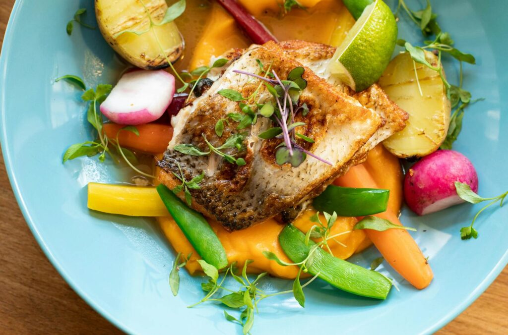 Colorful salmon dish with fresh vegetables on a blue plate, perfect for gourmet cuisine lovers.