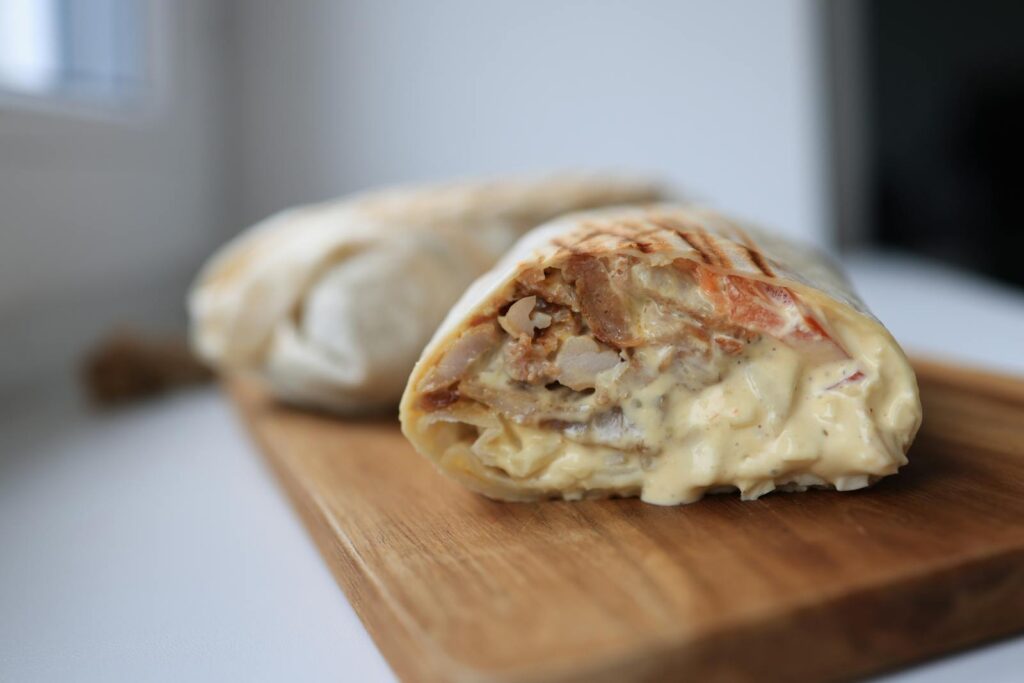 Tasty chicken wrap filled with creamy sauce on a wooden cutting board.