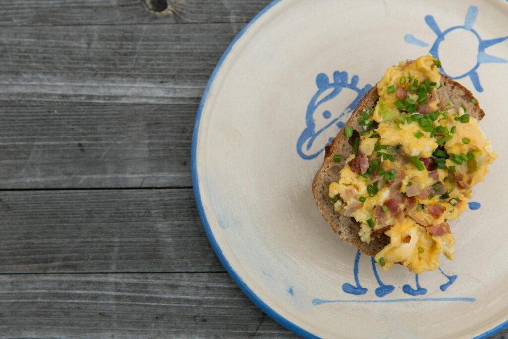 Delicious scrambled eggs with ham and chives on toast, served on a whimsical plate.