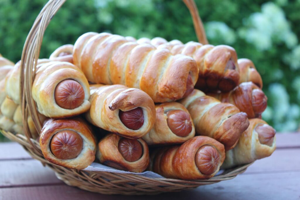 A close-up shot of freshly baked sausage rolls in a basket, outdoors.