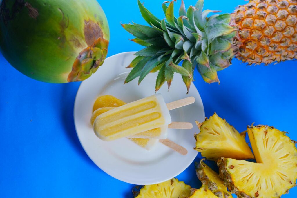 Refreshing pineapple and coconut popsicle with tropical fruits on a vibrant blue backdrop.