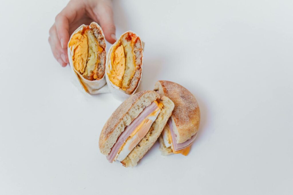 Delicious egg and cheese breakfast sandwiches with hand reaching, showcasing a fresh meal.