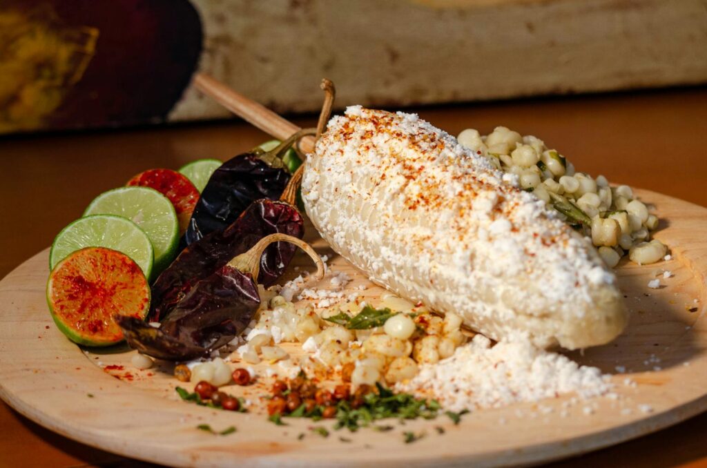 Delicious Mexican street corn, elote, served with chili, lime, and cheese toppings on a wooden plate.
