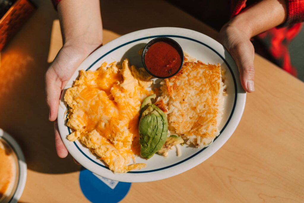 Plate of cheesy scrambled eggs, avocado, hash browns, and sauce, perfect for breakfast.