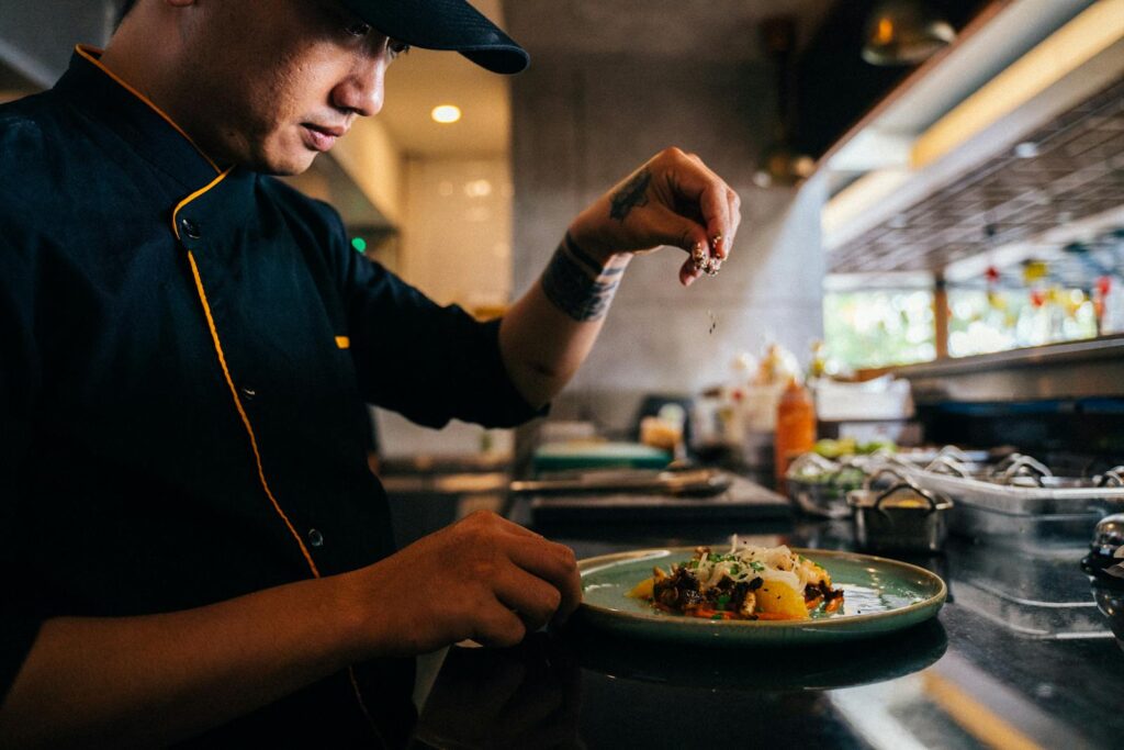 Chef skillfully sprinkles seasoning on a beautifully presented gourmet dish in a professional kitchen.