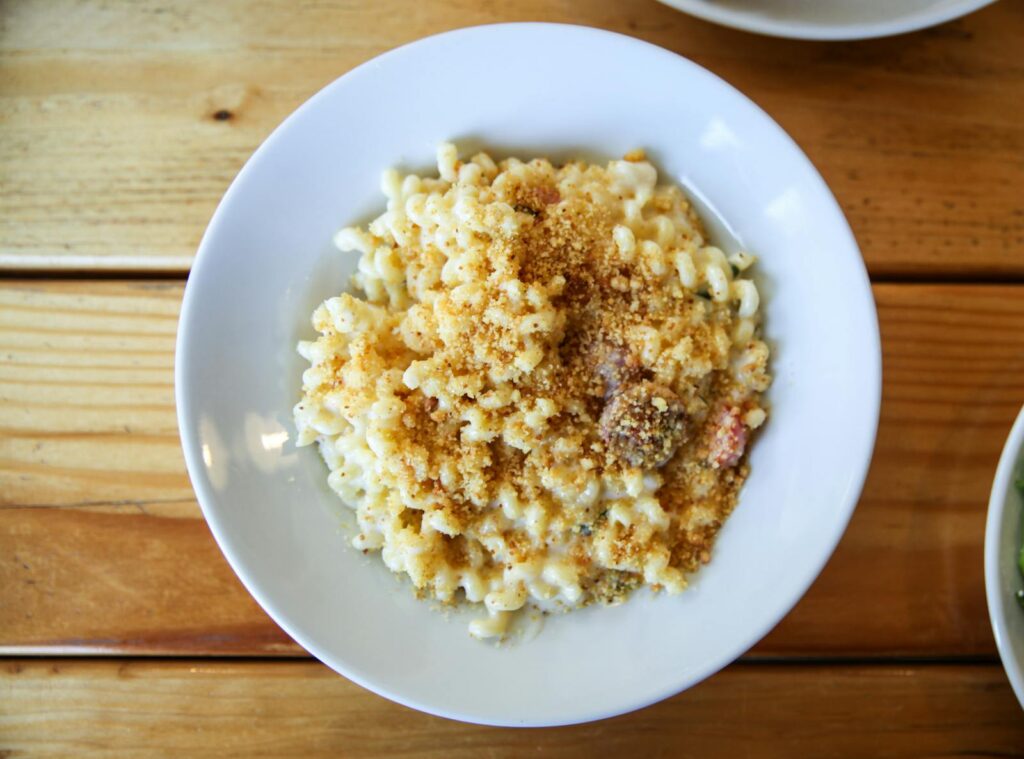 A close-up of creamy mac and cheese with breadcrumbs in a white bowl on a wooden table.