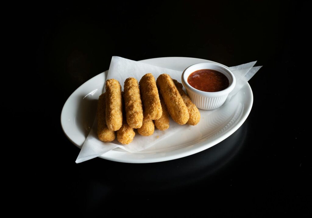 Golden mozzarella sticks served with a side of tangy marinara sauce on a white plate.