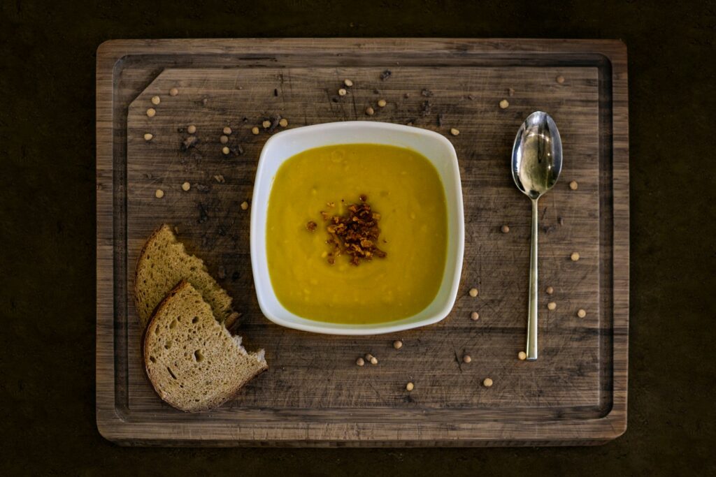 yellow soup in white ceramic bowl beside stainless steel spoon