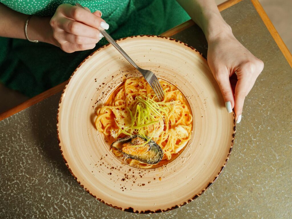Top view of a woman enjoying creamy pasta on a wooden plate.