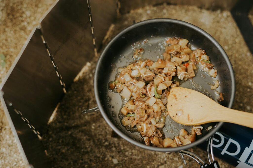 Top view of diced vegetables being cooked in a pan with wooden spoon outdoors.