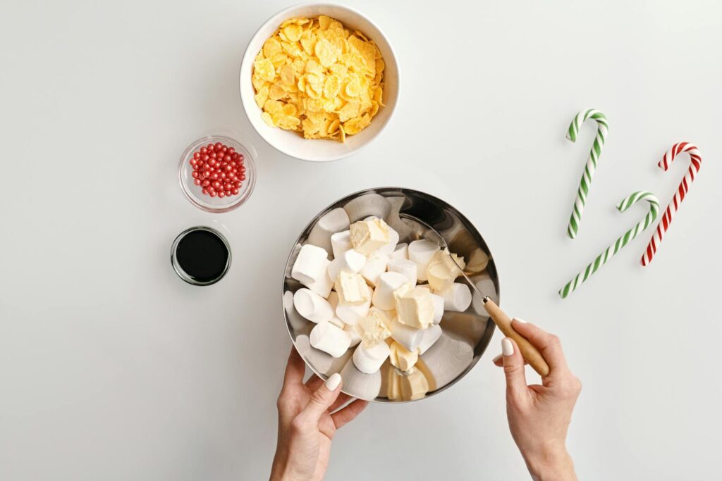 Flat lay of marshmallow and butter ingredients for Christmas baking with candy canes and cereal.