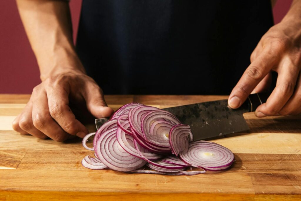 Close-up of hands slicing a red onion on a wooden chopping board, ideal for cooking content.