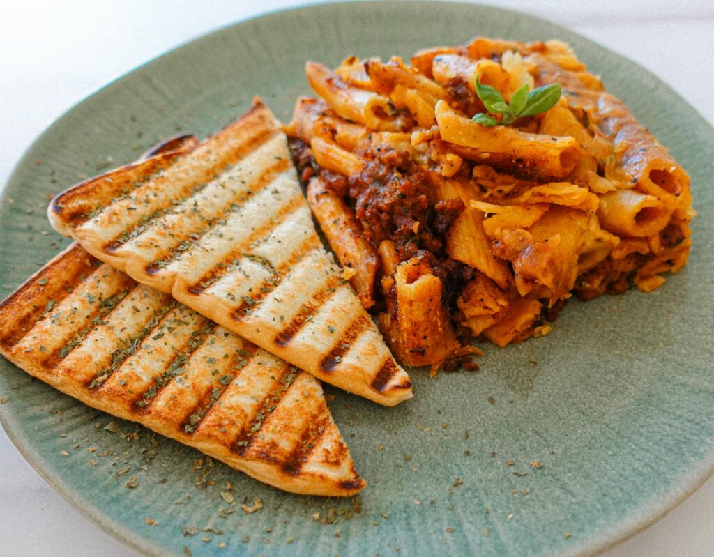 Appetizing cheesy penne paired with grilled bread on a rustic green plate, perfect for Italian cuisine lovers.