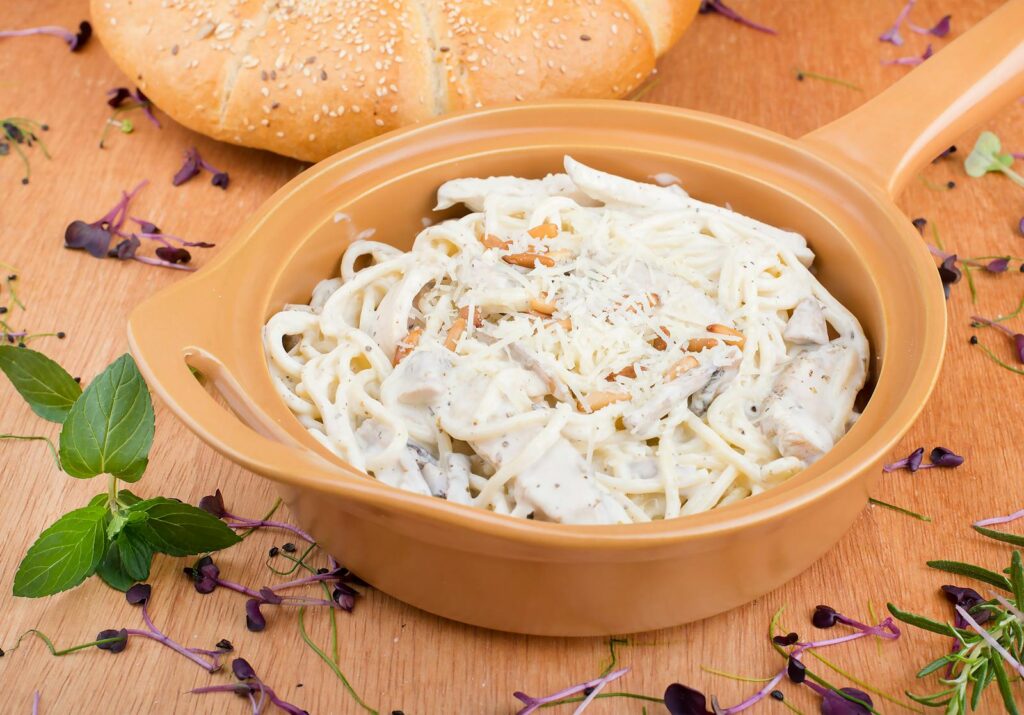 Delicious creamy pasta in a tan dish, garnished with fresh herbs, perfect for lunch or dinner.