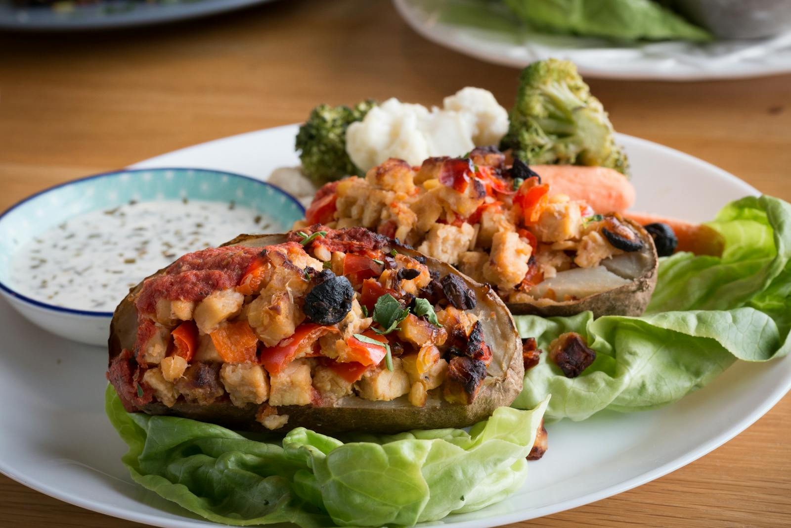 Tasty stuffed baked potato with assorted vegetables and sauce on a white plate.