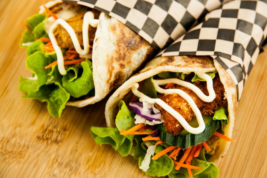 Close-up of chicken wraps with lettuce, cucumber, carrots, and mayo on wooden surface.
