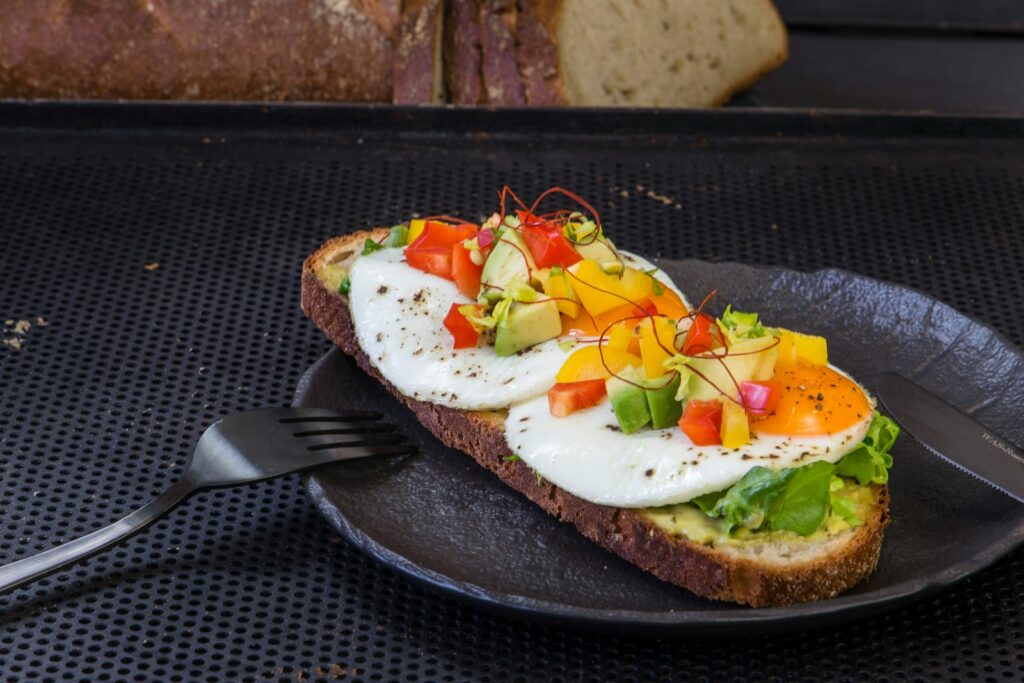 a black plate topped with a piece of bread covered in eggs and veggies